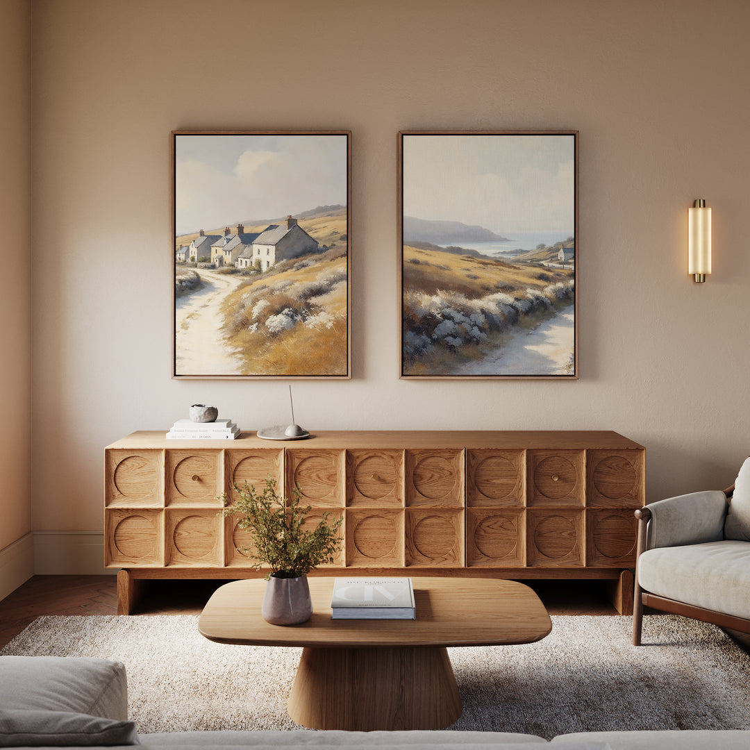 A cozy living room with rustic charm features a wooden coffee table, modern sideboard, neutral armchairs, and the Coastal Haven - Set of 2 canvas prints above. A wall sconce provides soft lighting.