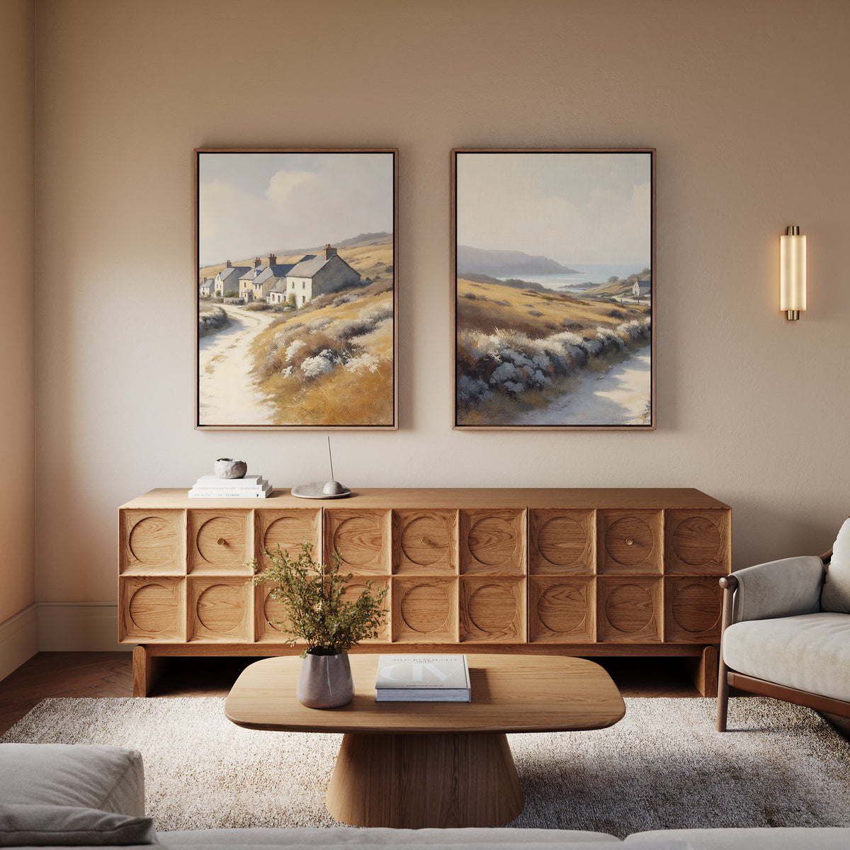 A cozy living room with rustic charm features a wooden coffee table, modern sideboard, neutral armchairs, and the Coastal Haven - Set of 2 canvas prints above. A wall sconce provides soft lighting.