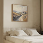 A cozy bedroom features a beige bed with white pillows and the "Coastal Haven Canvas Art - Square" above the headboard, adding minimal, soft-toned décor with rustic charm.