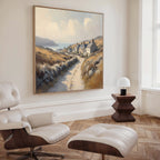 A modern living room with a white lounge chair and ottoman, wooden side table with a small white lamp, and the Coastal Haven Canvas Art - Square hanging on the wall.