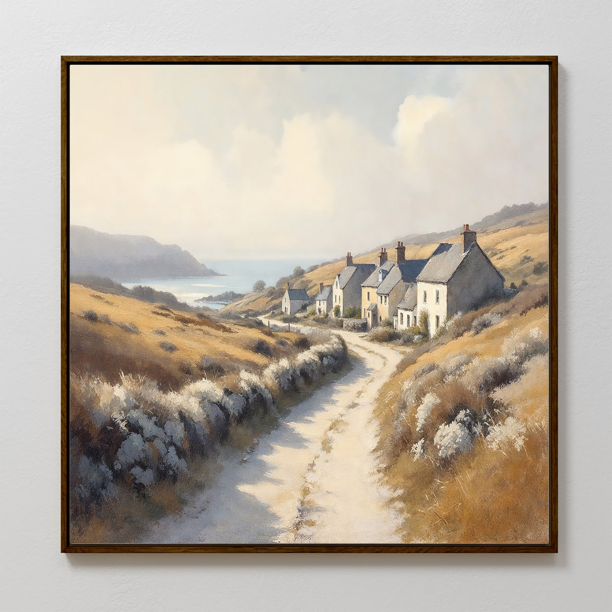 The Coastal Haven Canvas Art - Square features a framed print of a winding dirt road to stone cottages among golden hills, with sea and cliffs in the distance under a partly cloudy sky, adding rustic coastal charm to your space.