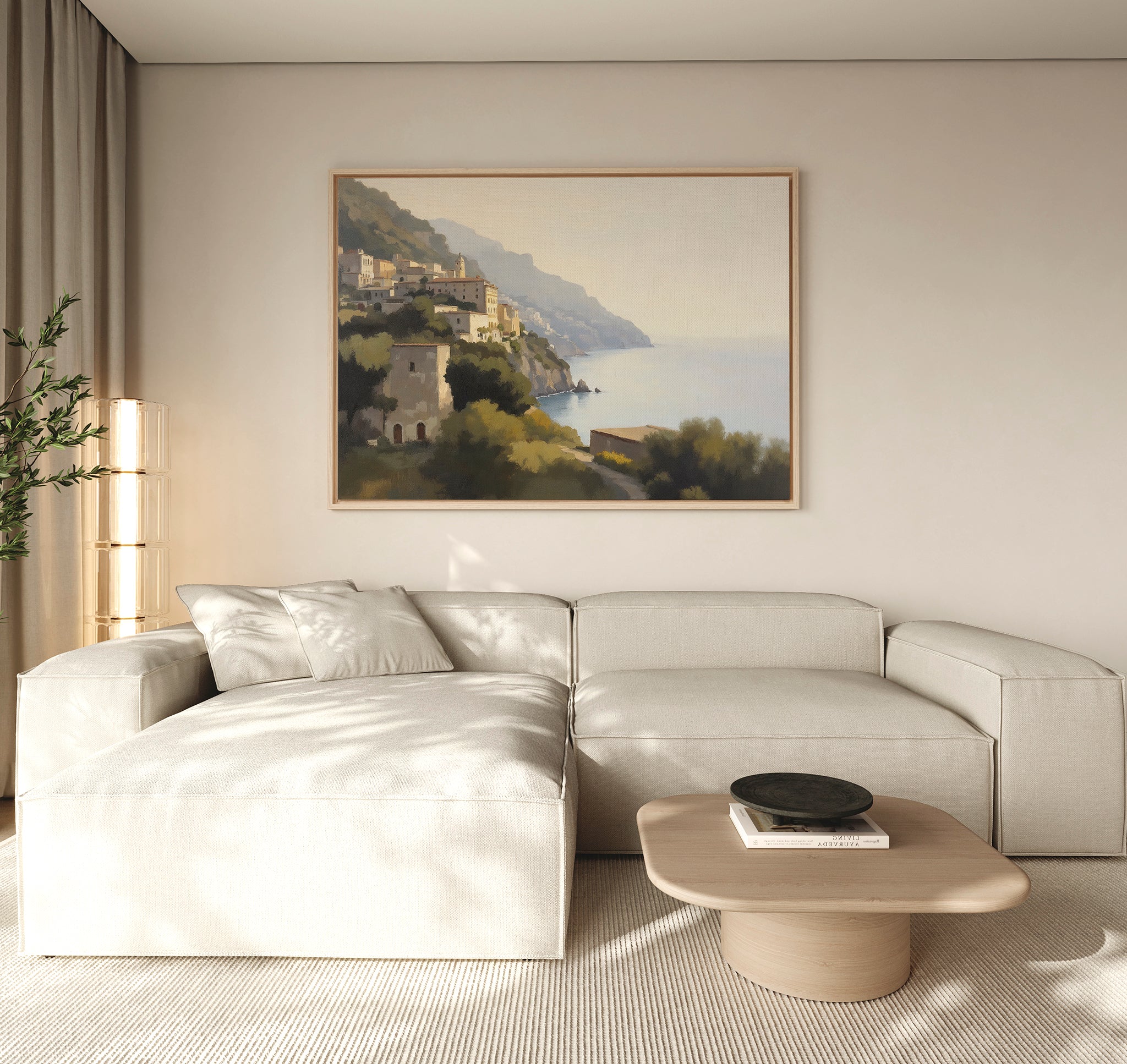 A modern living room with a light beige sectional sofa, round wooden coffee table, potted plant, and the Italian Reverie Canvas Art - Horizontal depicting a coastal village. Soft neutrals create a calm, inviting atmosphere.
