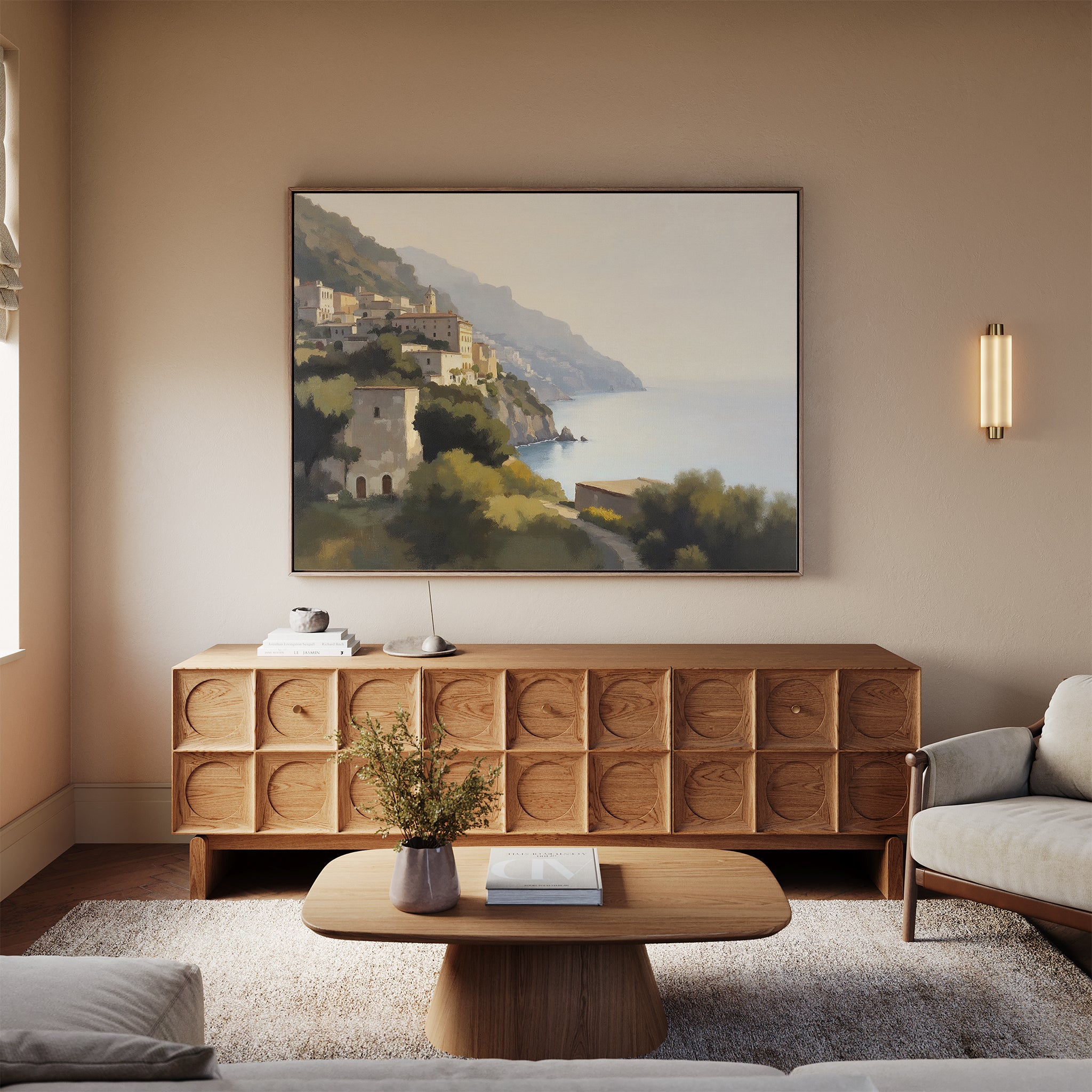 A cozy living room features a modern beige sofa, wooden coffee table, textured sideboard, and the Italian Reverie Canvas Art - Horizontal depicting coastal cliffs. Soft lighting and neutral tones enhance the inviting atmosphere.