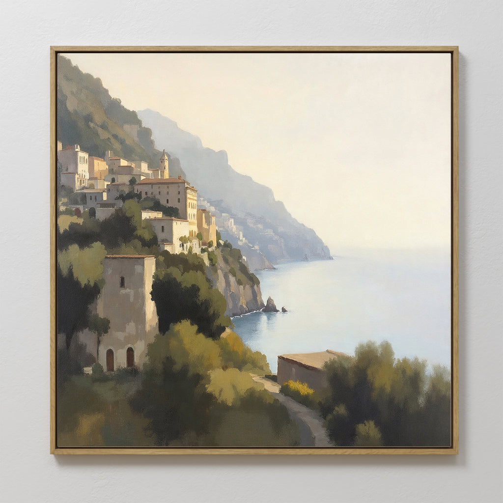 Italian Reverie Canvas Art - Square: A framed Mediterranean print depicting a coastal hillside village with sunlit buildings, lush greenery, and calm blue sea under a clear sky—the perfect touch of elegance for your home decor.