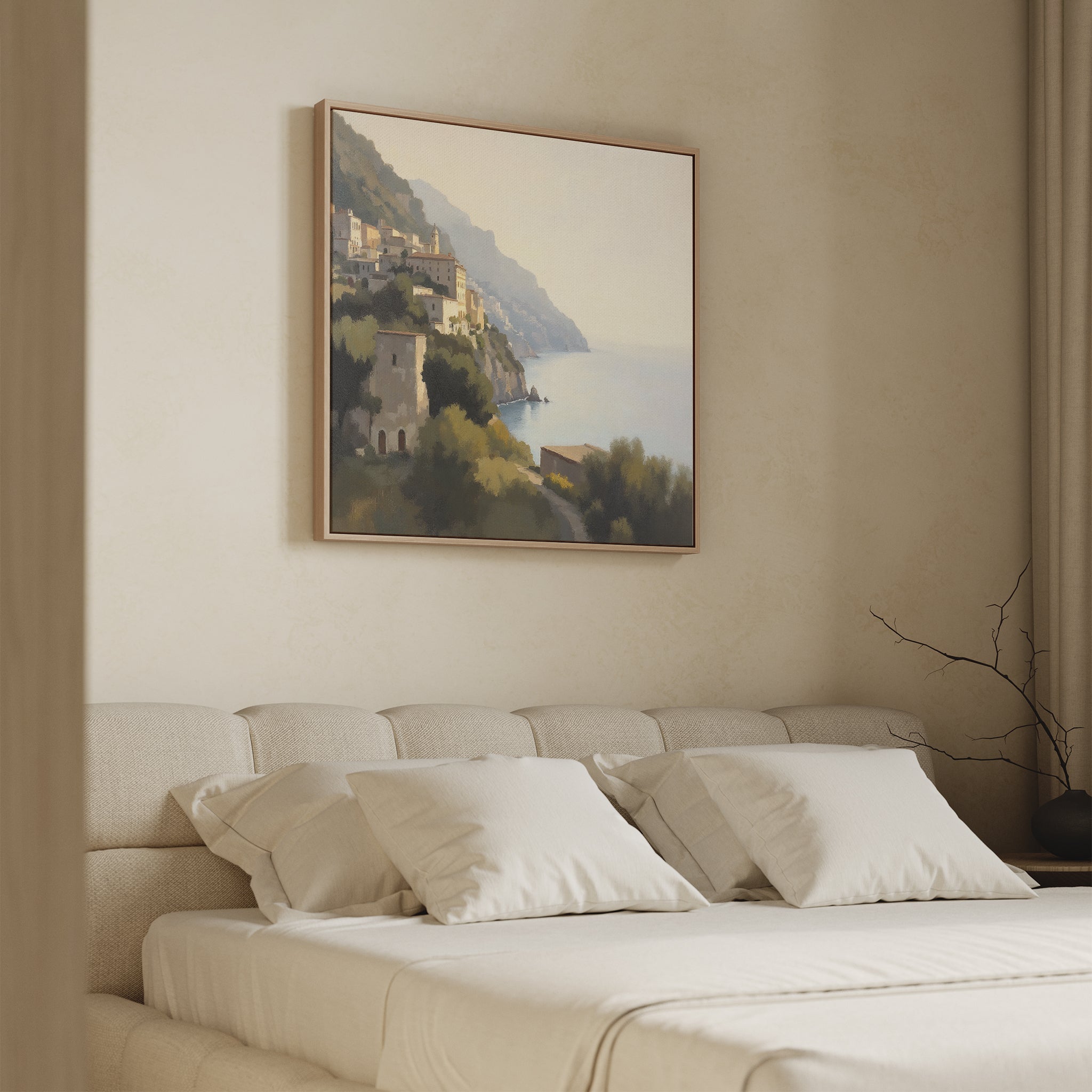 A beige, minimalist bedroom features a low upholstered bed with white pillows. Above, the Italian Reverie Canvas Art - Square depicts a Mediterranean village under a hazy sky, adding elegance. A bare branch graces the nightstand.