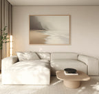 A minimalist living room features a light beige sectional, low wood coffee table, and the Coastal Silence Canvas Art - Horizontal depicting a misty beach. Muted coastal decor and soft lighting create a calm, serene ambiance.