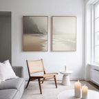 A bright, minimalist living room features a gray sofa, wooden chair, and the "Coastal Silence - Set of 2" wall art above. A small white side table with a candle and more candles on a round table by the window complete the serene Nordic Park vibe.
