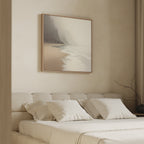 A minimal, neutral-toned bedroom features a tufted bed with cream bedding and "Coastal Silence Canvas Art - Square" above the headboard, depicting a foggy seashore and cliffs. A bare branch on the side table is lit by soft natural light.
