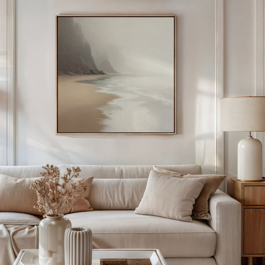 A neutral-toned living room features a beige sofa with cream pillows, a wooden side table with a white lamp, dried flowers in a vase, and the Coastal Silence Canvas Art - Square above the sofa for a serene, natural palette.