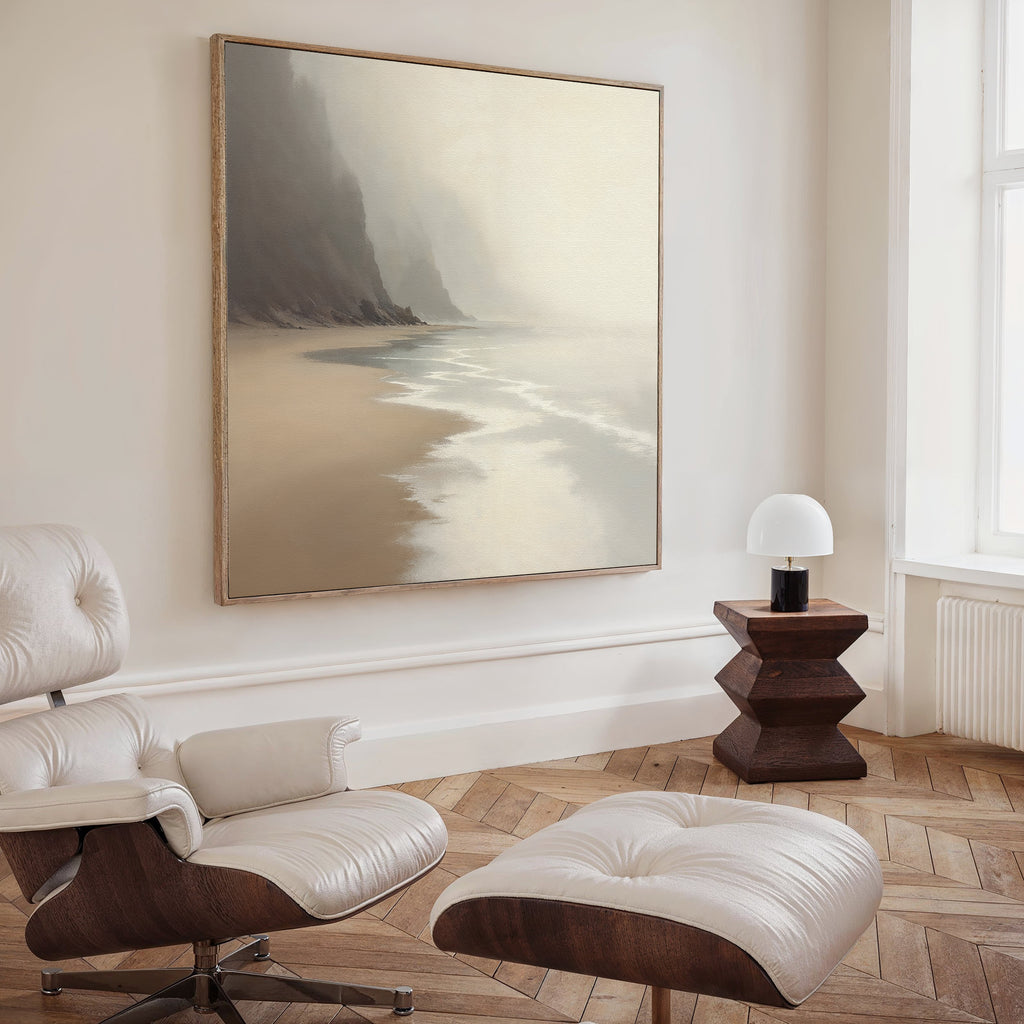 A cozy, modern room features a white leather lounge chair with ottoman, a wooden side table and small white lamp, and the Coastal Silence Canvas Art - Square in natural tones displayed on the wall above.