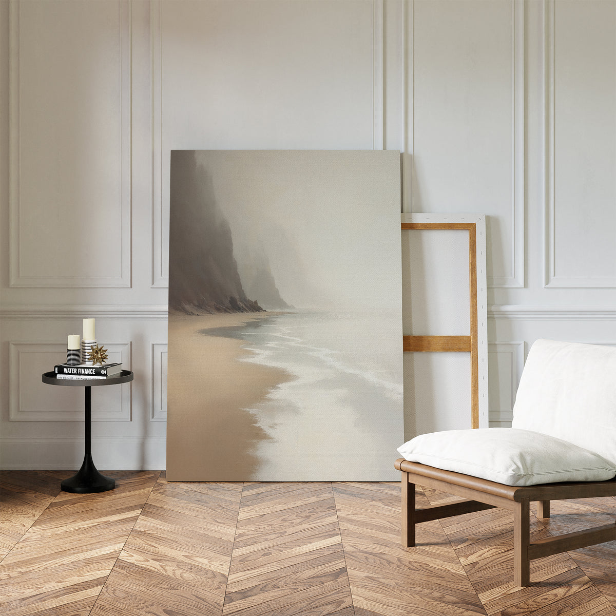 A minimalist room with herringbone wood floors, a white cushioned chair, a small round black table with candles and books, and the Coastal Silence Canvas Art - Vertical leaning against a white paneled wall.