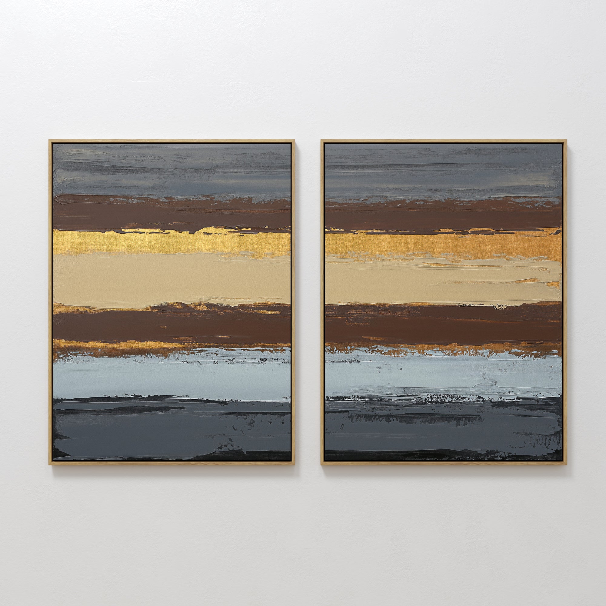 The "Coastal Strata - Set Of 2" features framed abstract prints with horizontal bands of gold, brown, blue, and gray tones, adding earthy sophistication to any space.