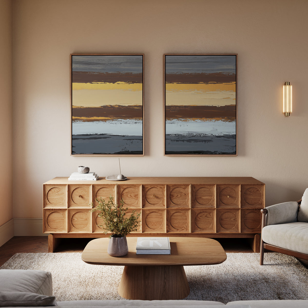 A cozy living room featuring a wooden sideboard, a low coffee table, a light armchair, and “Coastal Strata - Set Of 2” artwork prints with horizontal stripes on a beige wall. A small wall sconce adds soft, earthy sophistication.