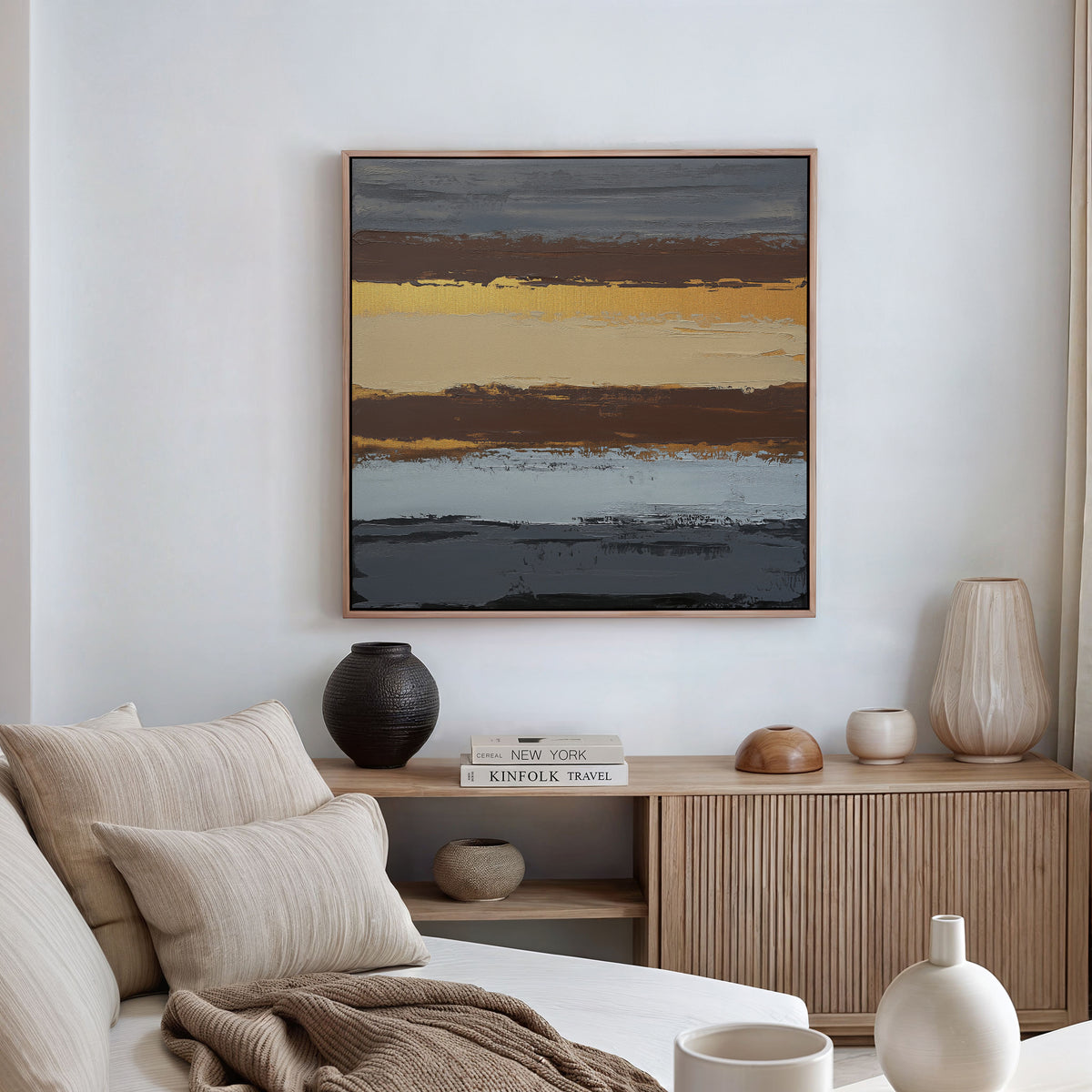 A modern living room with a beige sofa, neutral cushions, a wooden sideboard with vases and decor, and the Coastal Strata Canvas Art - Square, which adds earthy sophistication through abstract bands of yellow, brown, gray, and blue.