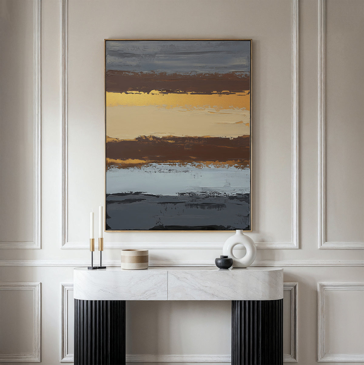 A modern entryway features a white marble console table with black ribbed legs, decorative objects, and the Coastal Strata Canvas Art - Vertical above, showcasing earthy sophistication with its bands of gray, gold, brown, and blue.
