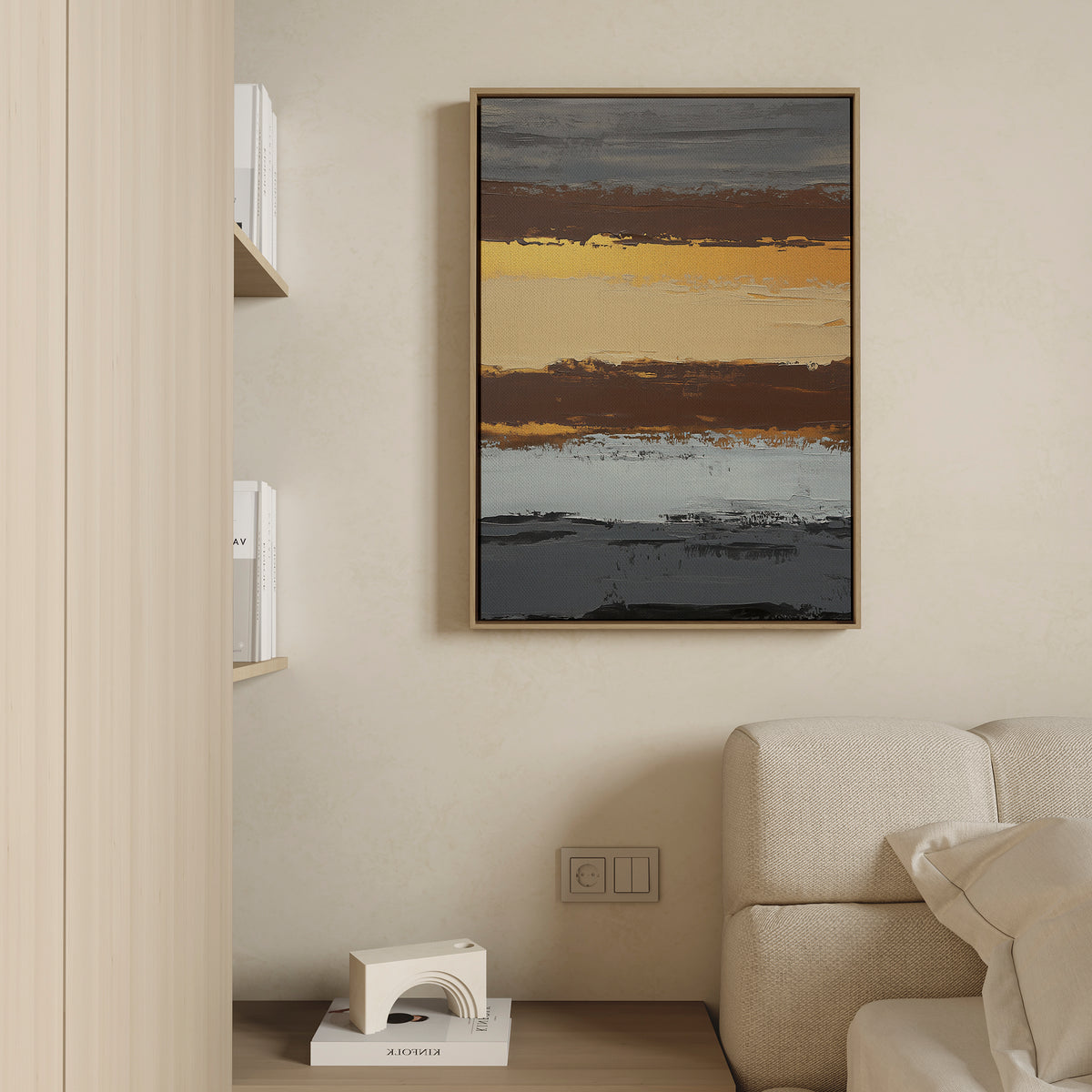 A modern living room with a beige sofa, light wood shelves of books, and the Coastal Strata Canvas Art - Vertical featuring gold, brown, blue, and gray stripes on a cream wall for an elegant touch of earthy sophistication.
