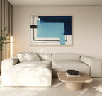 A modern living room features a light beige sectional sofa, a wooden coffee table with books and a black bowl, a tall plant, and the Cobalt Intersection Canvas Art - Horizontal in blue adding flair above the sofa.