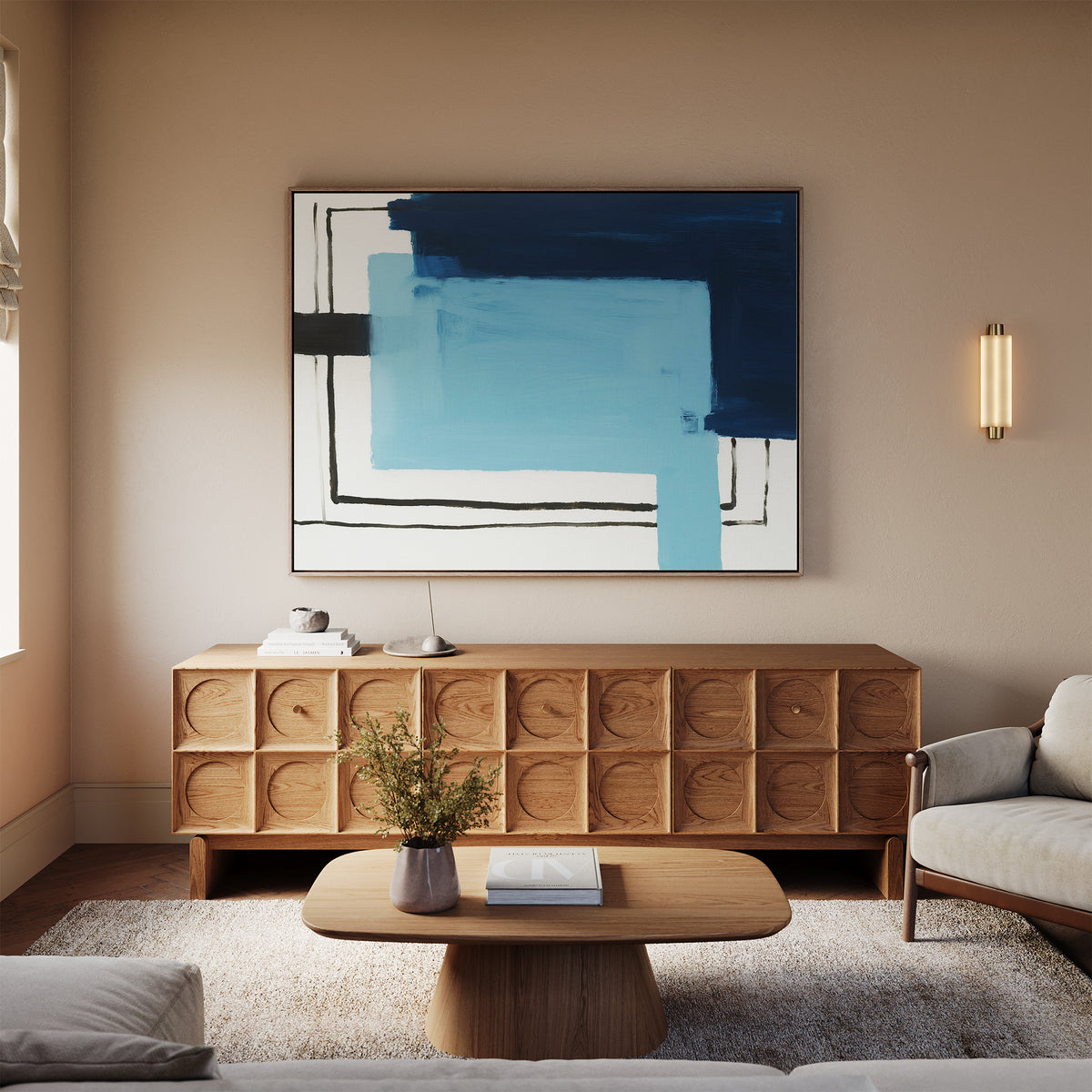 A modern living room featuring a wooden cabinet, the Cobalt Intersection Canvas Art - Horizontal in blue and black, a beige sofa, wooden coffee table with books, small plant, and soft natural light—a perfect blend of modern decor.