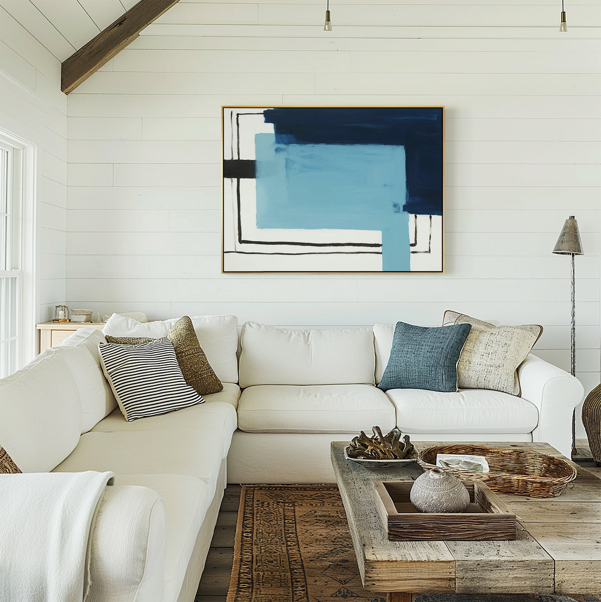 A bright living room with a white sectional sofa, neutral and blue pillows, a rustic wooden coffee table, and Cobalt Intersection Canvas Art - Horizontal on white shiplap walls. Sunlight from the left enhances the modern decor.