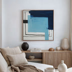 A modern living room featuring a light wood sideboard, neutral decor, and a white sofa with beige pillows. On the wall is the Cobalt Intersection Canvas Art - Square, a contemporary abstract print in blue, black, and white.