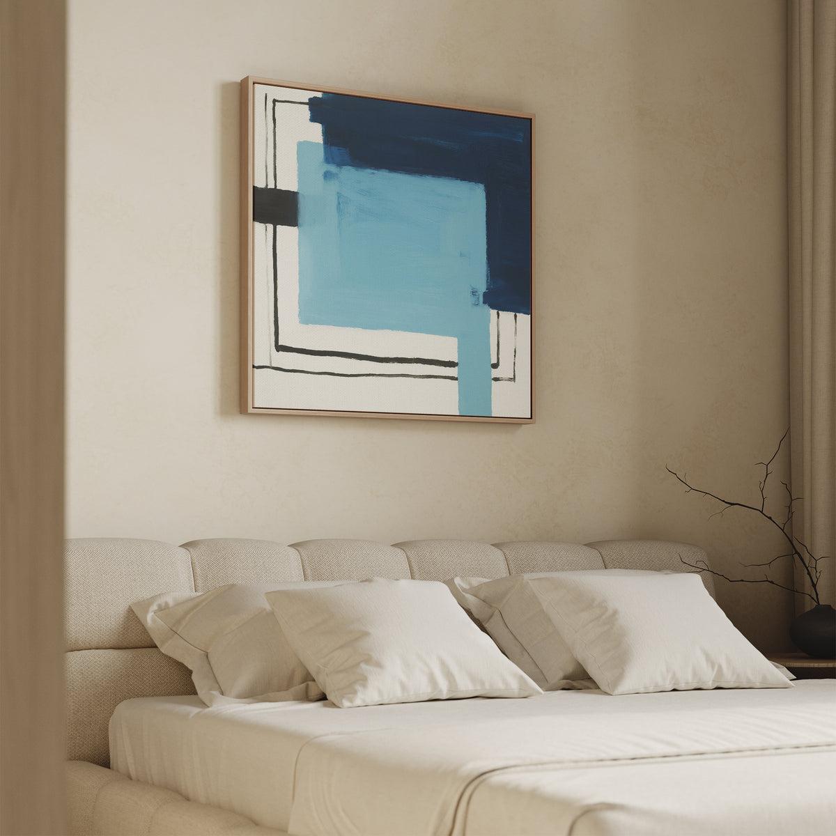 A beige bedroom features a tufted headboard, white bedding, and pillows. Above the bed hangs the Cobalt Intersection Canvas Art - Square, showcasing blue geometric shapes and black lines. A bare branch sits on a side table by the window.