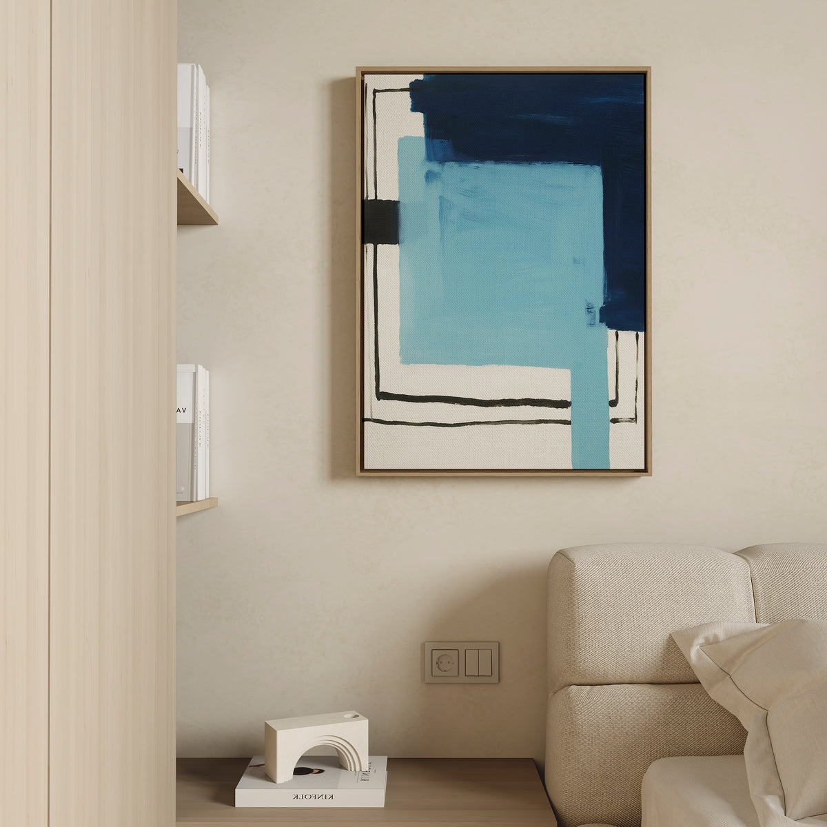 A minimalist living room includes a beige sofa, a wooden shelf with books and a small white decor piece, and the Cobalt Intersection Canvas Art - Vertical in blue and black tones displayed on a light-colored wall.