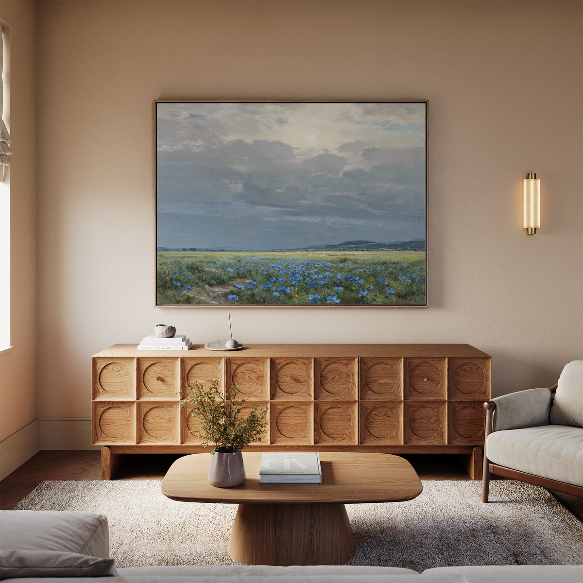 A cozy living room with a light sofa, wooden coffee table, and circular-patterned sideboard. Above the sideboard hangs the Cornflower Fields Canvas Art - Horizontal, adding countryside charm. A vase with flowers and books rest on the table.