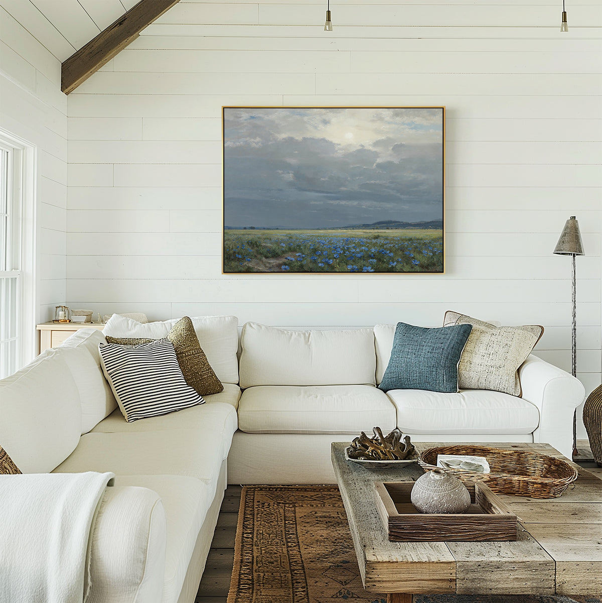 A bright living room featuring a white sectional sofa, textured pillows, a rustic wooden coffee table, and the Cornflower Fields Canvas Art - Horizontal on white shiplap walls brings countryside home decor charm.
