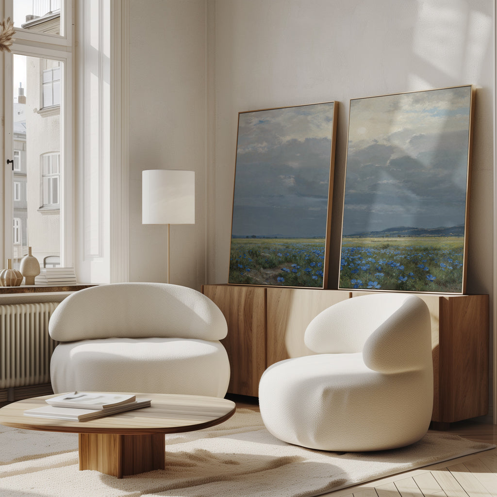 A modern living room with two rounded white chairs, a low wooden coffee table, a floor lamp, and Cornflower Fields - Set of 2 canvas prints on a wooden sideboard, all illuminated by natural light from tall windows.