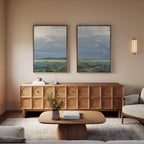A cozy living room with a wooden sideboard, a light-colored sofa, a wooden coffee table with books, a plant, and a modern wall sconce. Above the sideboard hang Cornflower Fields - Set of 2 canvas prints for calm, minimalist decor.