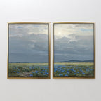 The Cornflower Fields - Set of 2 features framed canvas prints showing a pastoral landscape with wide cornflower fields, distant hills, and soft sunlight filtering through clouds against a white wall.