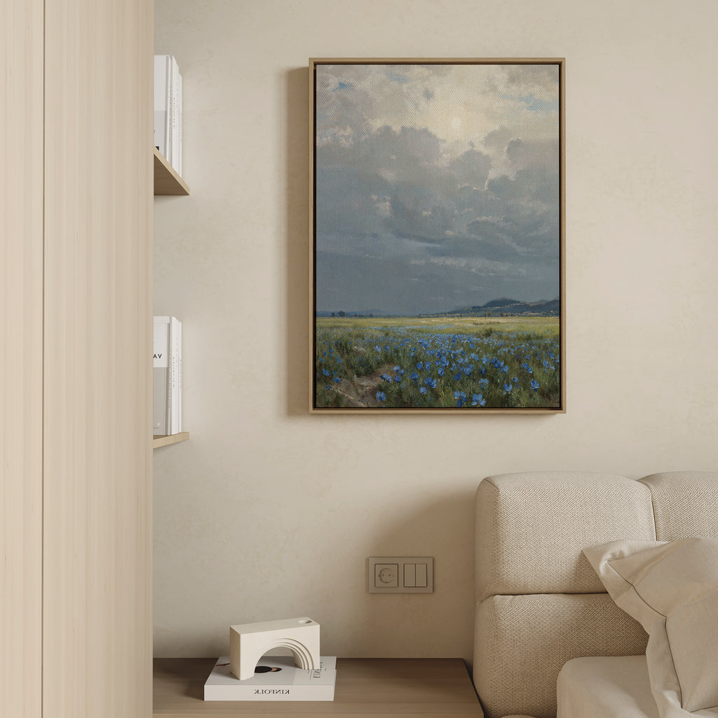 The Cornflower Fields Canvas Art - Vertical hangs on a beige wall above a light-colored sofa in a modern, minimalist living room, with shelves nearby holding books and a decorative object.