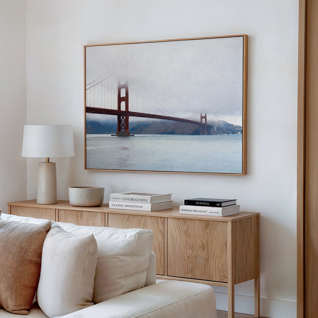 A modern living room showcases a wooden sideboard with books, a lamp, and decorative bowl. Above, the Crimson Passage Canvas Art - Horizontal adds coastal elegance to the white wall. A cream sofa sits in the foreground.