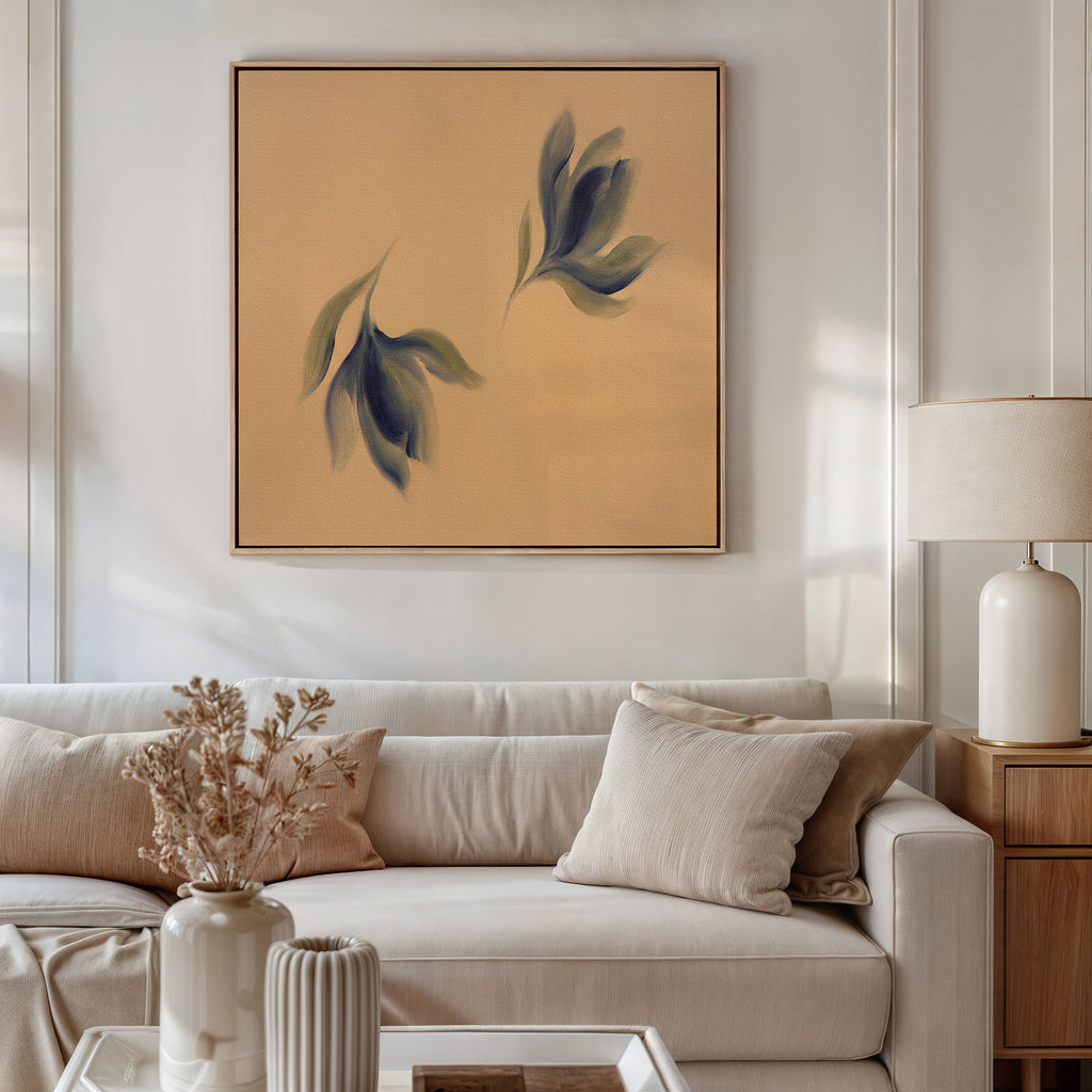 A modern living room features a beige sofa, neutral pillows, a lamp on a wooden side table, and dried flowers in a vase. Above the sofa hangs the Dancing Leaves Canvas Art - Square—abstract blue and green leaves on tan.