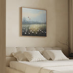 A beige bedroom with a cushioned bed, white pillows, and serene decor features the Dawn Meadow Canvas Art - Square above the headboard. Soft natural light and neutral accents create a calm, inviting atmosphere.