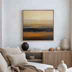 A modern living room features a light beige sofa, neutral cushions, and a wooden sideboard with vases. Above, the Desert Mirage Canvas Art - Square brings warm earth tones in an abstract style to the space.