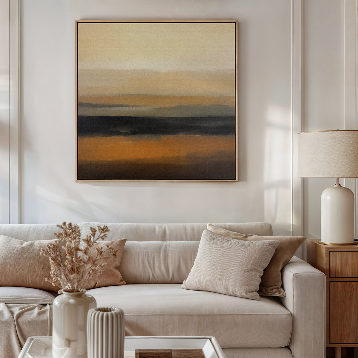 A modern living room with a light beige sofa, neutral cushions, a wooden side table with a ceramic lamp, dried flowers in a vase, and the Desert Mirage Canvas Art - Square in earthy tones hanging on the wall.