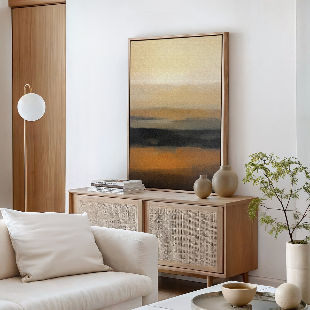 A modern minimal living room with a light wood console, desert earth tones, ceramic vases, books, a beige sofa with cushions, a round floor lamp, a potted plant, and the Desert Mirage Canvas Art - Vertical as an abstract focal point.