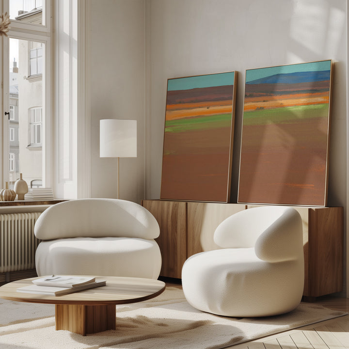 A modern living room with two white, rounded armchairs, a low wooden coffee table, and the "Desert Plains - Set of 2" canvas prints resting on a wooden sideboard against a bright window.