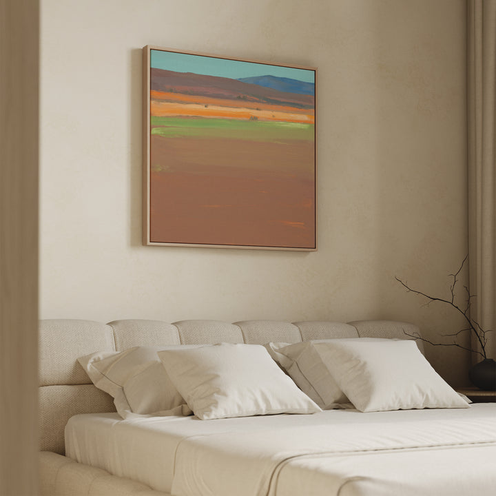 A modern bedroom features a beige upholstered bed with white bedding and four pillows. Above the bed hangs the Desert Plains Canvas Art - Square. A minimalist vase with twigs on the bedside table enhances the calm atmosphere.