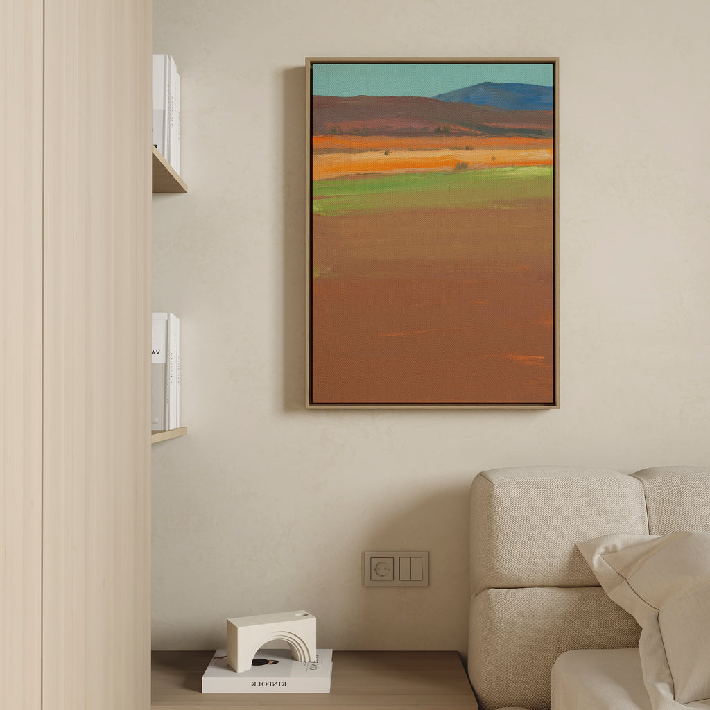 A modern living room with a beige sofa, built-in shelf with books, and the Desert Plains Canvas Art - Vertical—an abstract landscape featuring earthy tones and blue mountains—brings the perfect touch of southwestern wall art.