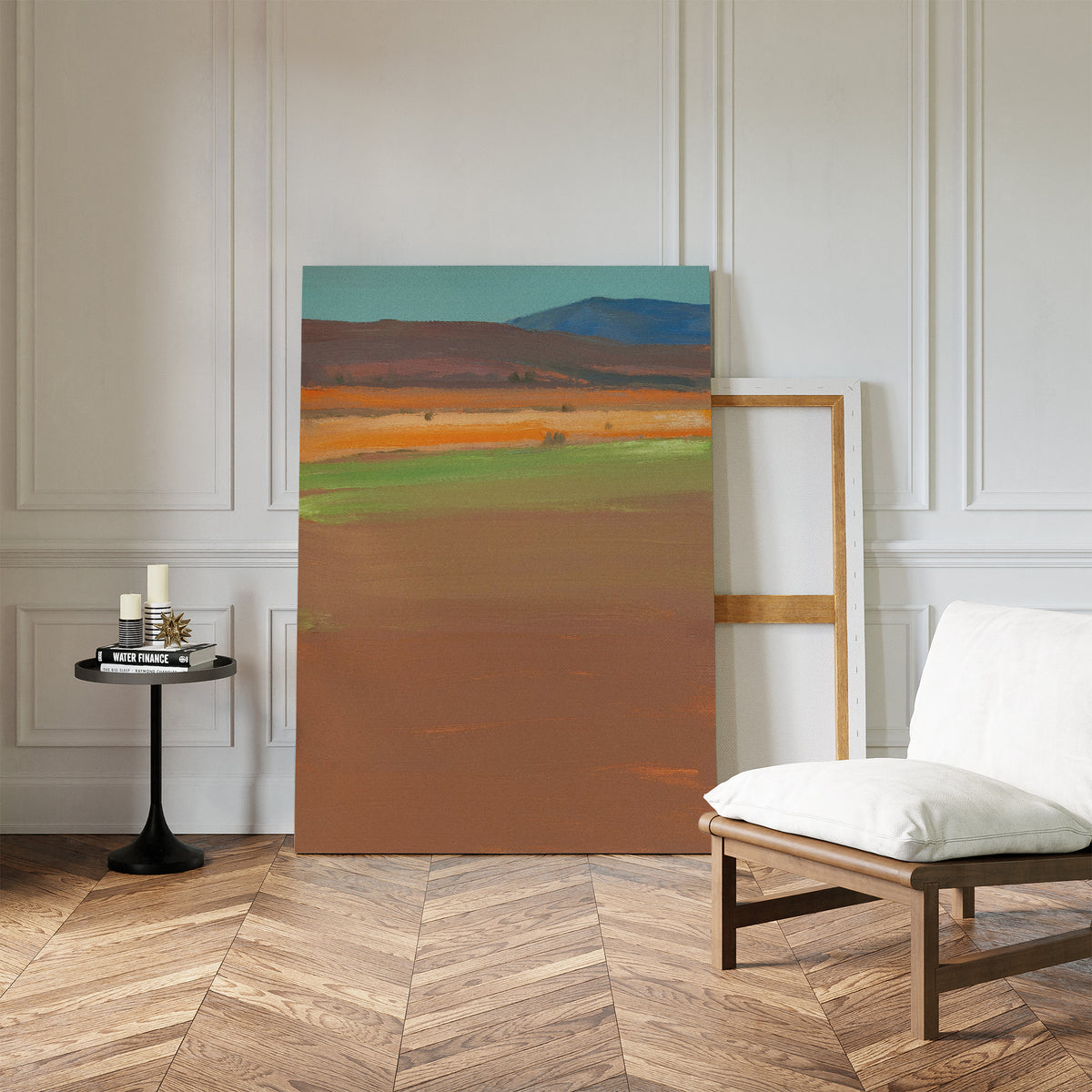 The Desert Plains Canvas Art - Vertical leans against a white paneled wall on a wooden herringbone floor, with a cushioned chair and small round black table holding candles and books completing this modern living room decor.