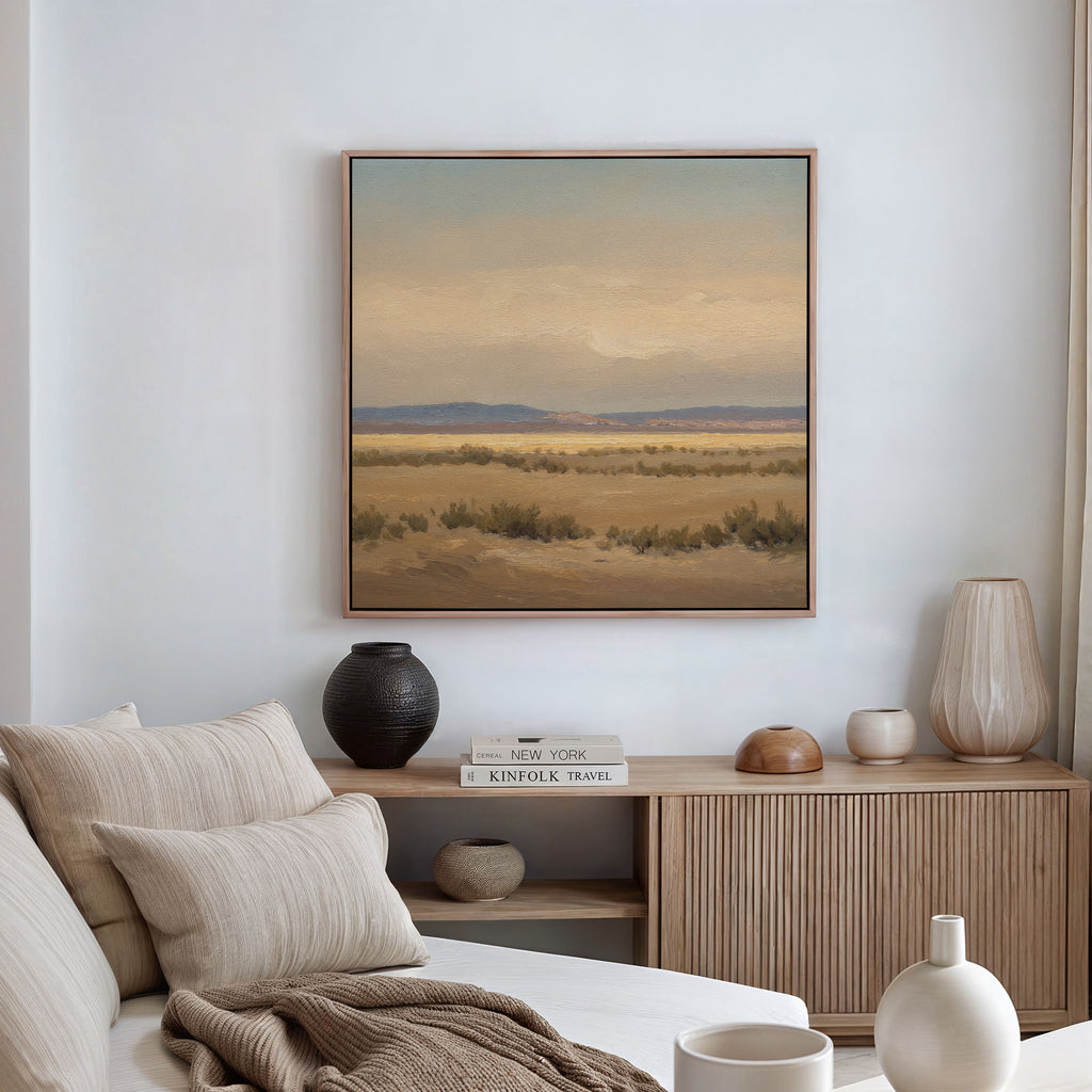 A cozy living room with a beige sofa, neutral pillows, wooden console table, vases, books, and the Desert Solitude Canvas Art - Square on the wall showcasing a southwestern landscape of fields and mountains.