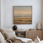 A cozy living room with a beige sofa, neutral pillows, wooden console table, vases, books, and the Desert Solitude Canvas Art - Square on the wall showcasing a southwestern landscape of fields and mountains.