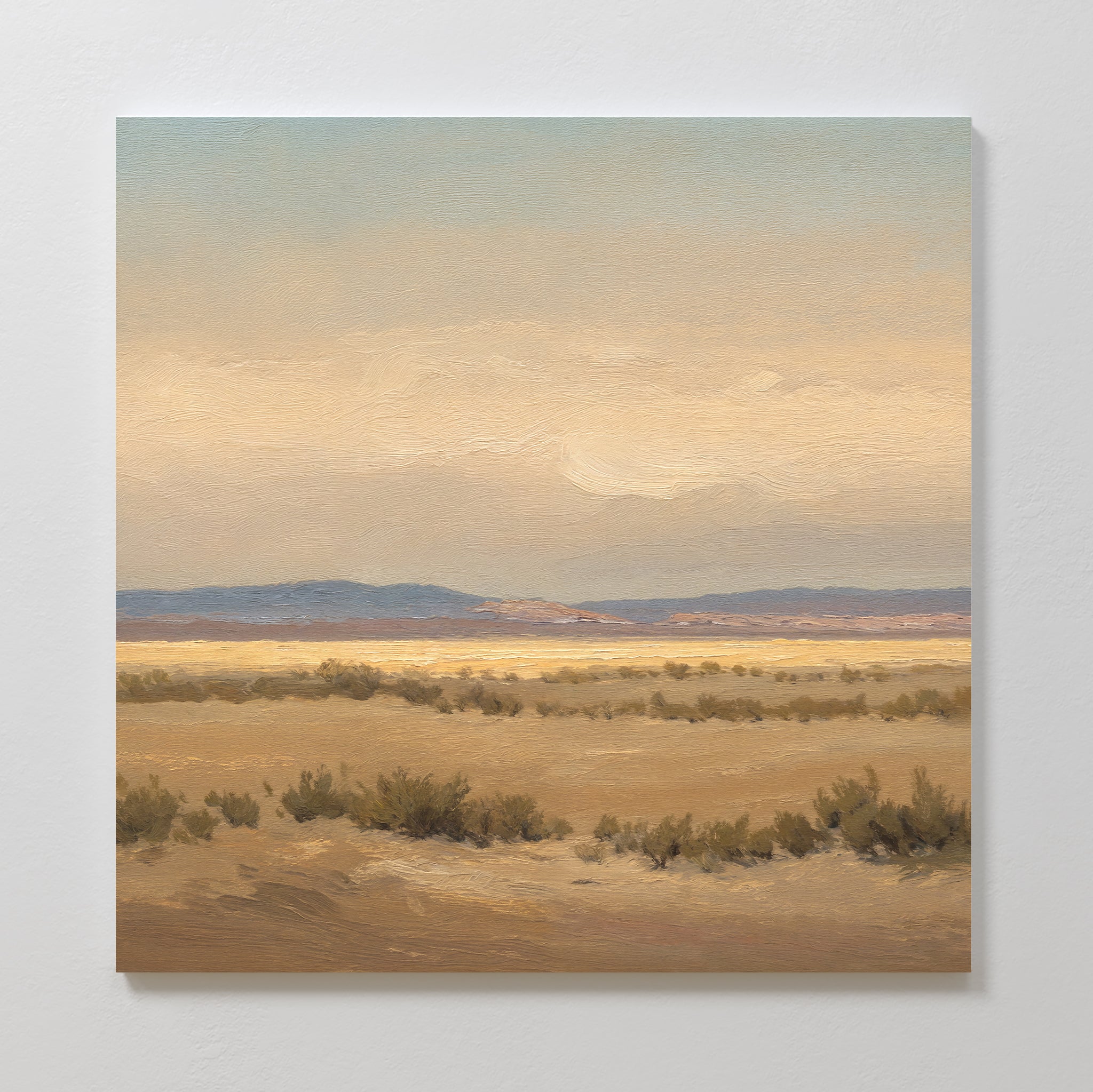 Desert Solitude Canvas Art - Square features a painted southwestern landscape with flat desert, low shrubs, distant hills, and a soft, cloudy sky in beige and blue—ideal serene wall decor for a calm, expansive atmosphere.