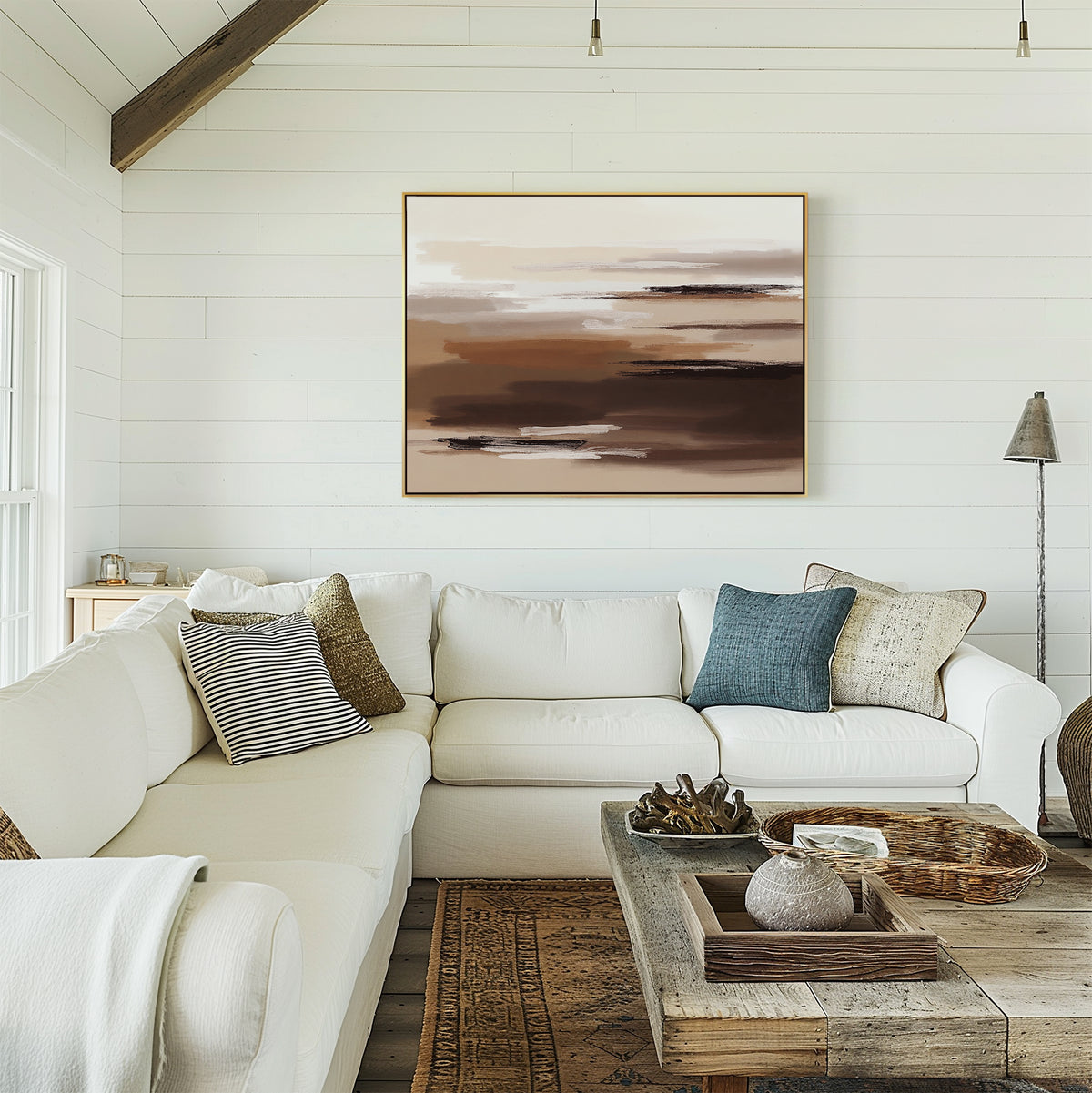 A bright living room with white shiplap walls, a large white sectional, assorted cushions, a rustic wooden coffee table, and the Desert Winds Canvas Art - Horizontal in earthy abstract tones displayed above the sofa.