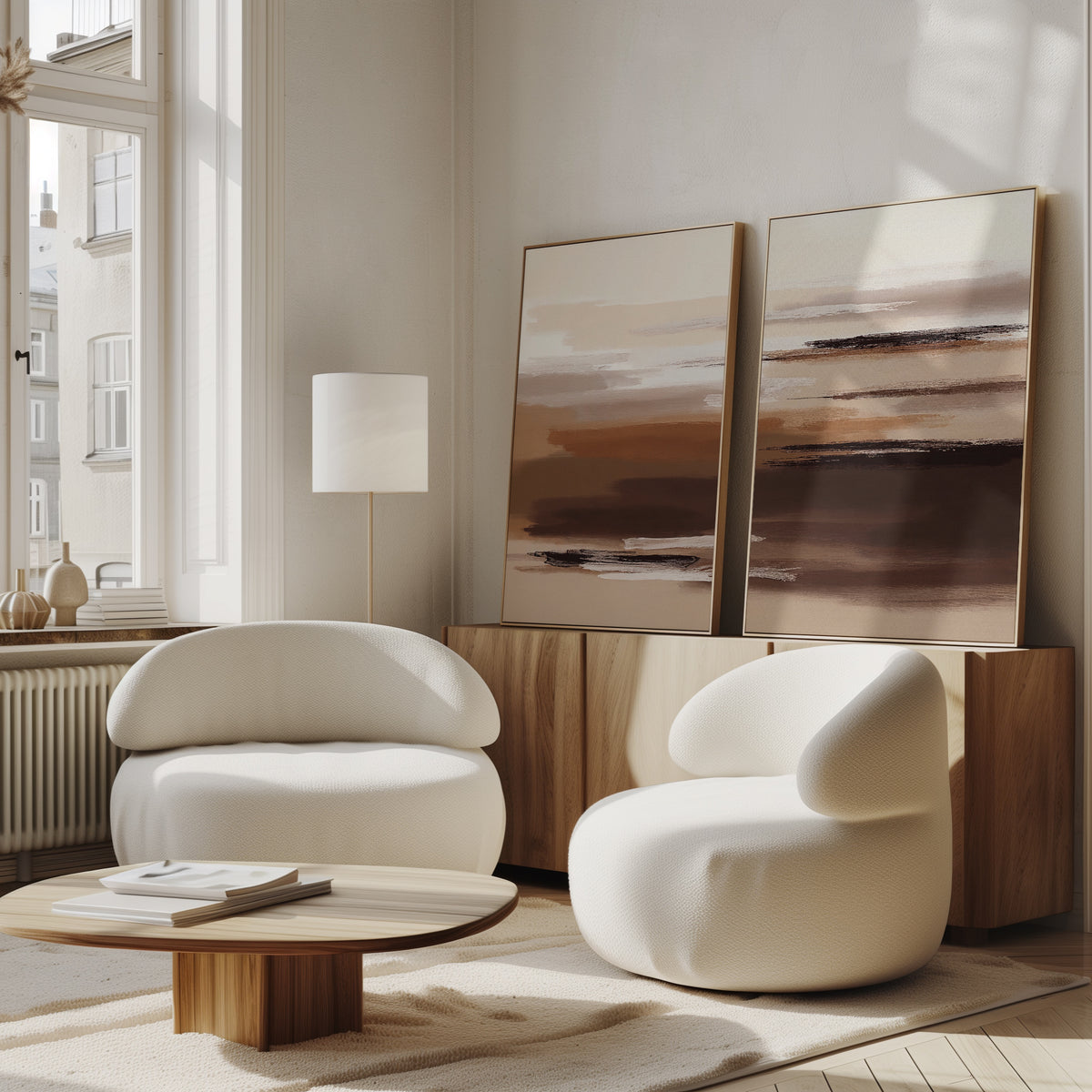 A modern living room featuring the Desert Winds - Set Of 2 white curved armchairs, a round wooden coffee table, and earth-toned artwork on a wooden sideboard. Large windows bathe the space in natural light.