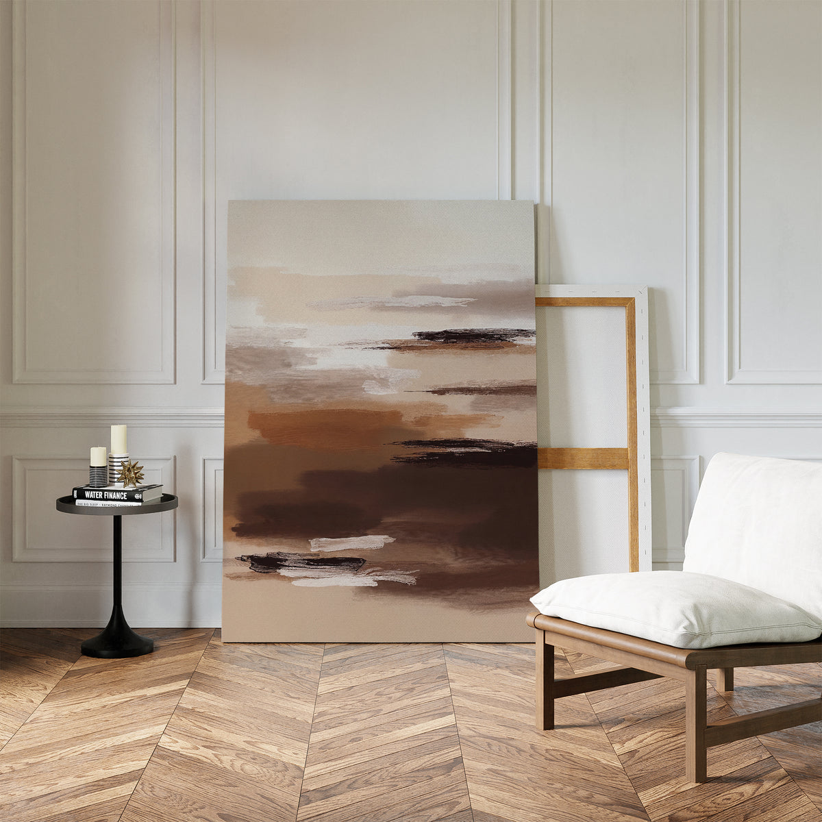 A minimal room with white paneled walls, herringbone wood floors, a cushioned wooden chair, a small round black side table with candles and books, and the Desert Winds Canvas Art - Vertical adds an earthy Nordic Park-inspired touch.
