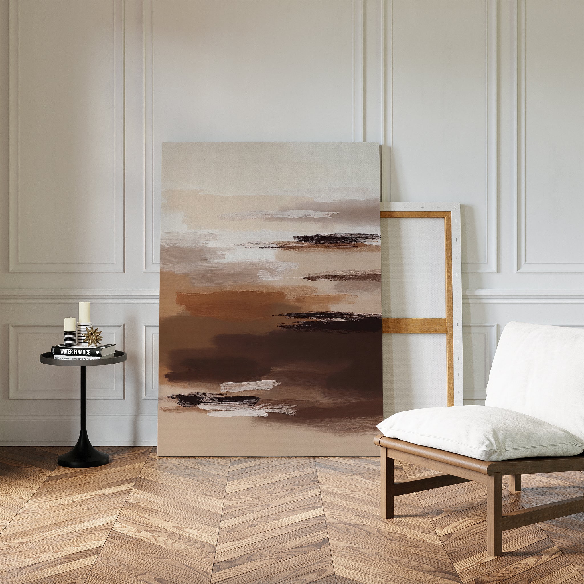 A minimal room with white paneled walls, herringbone wood floors, a cushioned wooden chair, a small round black side table with candles and books, and the Desert Winds Canvas Art - Vertical adds an earthy Nordic Park-inspired touch.