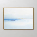 The Distant Archipelago Canvas Art - Horizontal features soft blue and white tones, a hazy horizon with warm yellow accents near the center, and is framed in thin gold, displayed on a plain white wall.